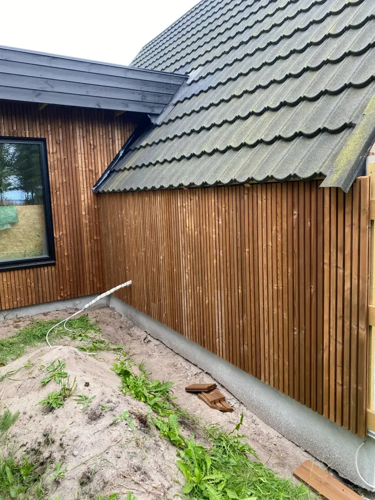 Træbeklædt hus med sort tegltag og have